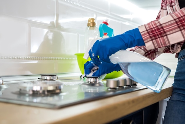 Foto mujer limpieza de superficie de gas de acero inoxidable en la cocina con guantes de goma.