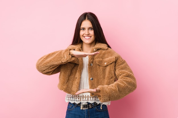 Mujer linda joven que lleva a cabo algo con ambas manos, presentación del producto.