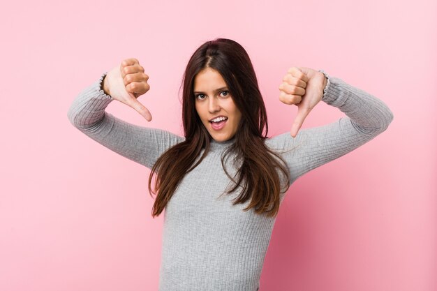 Mujer linda joven que muestra el pulgar hacia abajo y que expresa aversión.