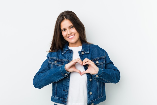 Mujer linda joven que sonríe y que muestra una forma del corazón con las manos.