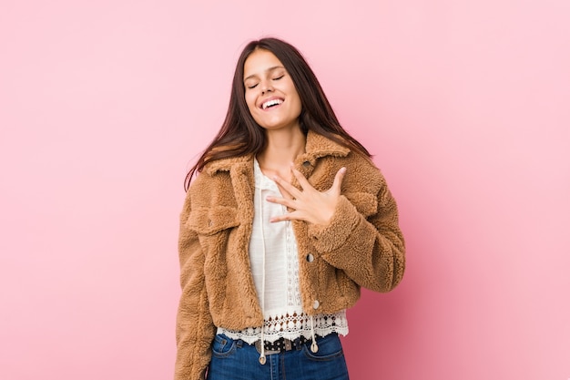 La mujer linda joven se ríe a carcajadas manteniendo la mano en el pecho.