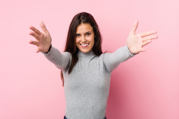 La mujer linda joven se siente confiada dando un abrazo a la cámara.