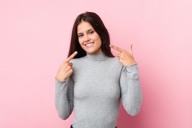 La mujer linda joven sonríe, señalando los dedos en la boca.