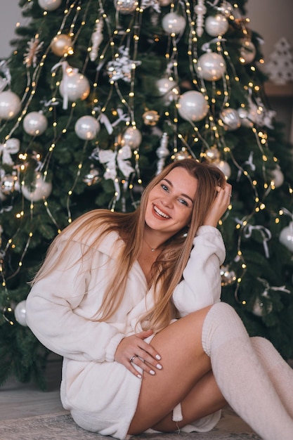 Una mujer linda se sienta cerca de un árbol de Navidad sonriendo esperando las vacaciones