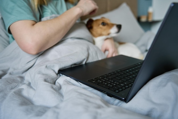 Mujer con un lindo perro acostado en la cama y usando una laptop por la mañana