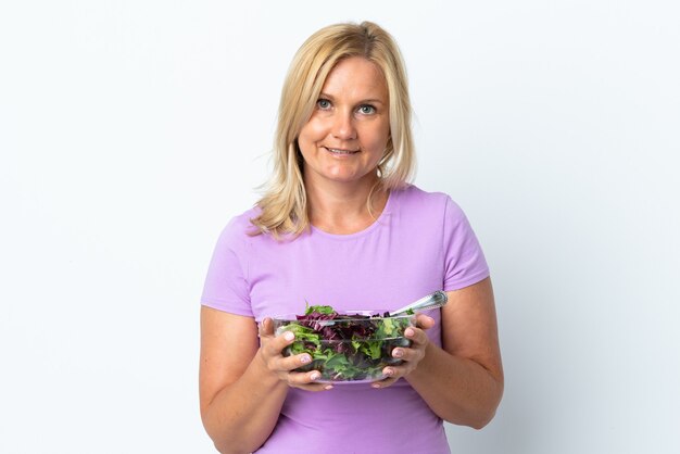 Mujer lituana de mediana edad aislada sobre pared blanca sosteniendo un plato de ensalada con expresión feliz