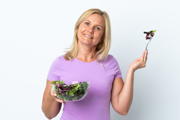 Mujer lituana de mediana edad aislada sobre pared blanca sosteniendo un plato de ensalada con expresión feliz