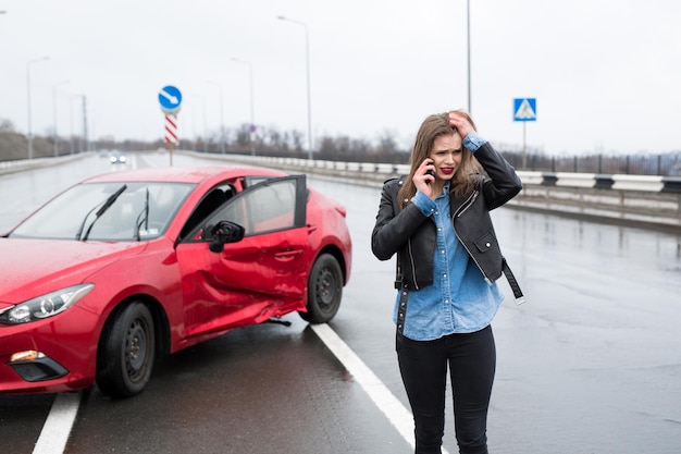 Mujer llama a un servicio de pie junto a un coche rojo