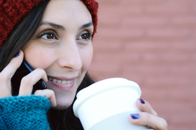 Mujer llamando en el teléfono móvil y sosteniendo una taza de café.