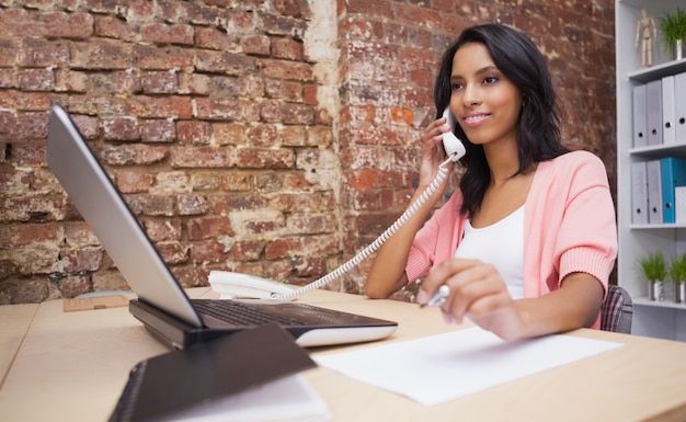 Mujer llamando y usando la computadora portátil sentado en su escritorio