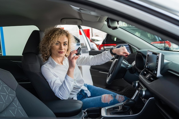 Mujer con llave sentada en un coche nuevo en el concesionario