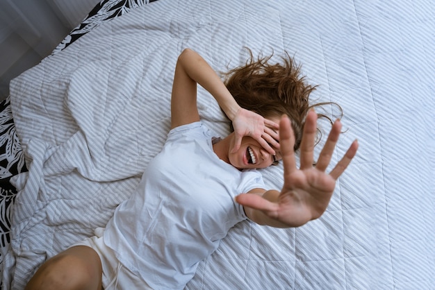 Mujer llena de alegría en pijama estirando los brazos después de despertarse acostado en una cama acogedora feliz sonriendo un ...