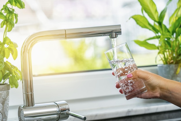 Mujer llenando un vaso con agua del grifo en la cocina