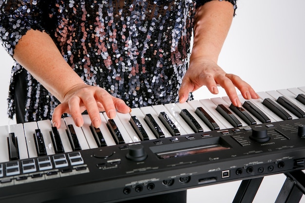 Una mujer lleva una blusa brillante y está posando con un teclado de piano. Aislado en blanco