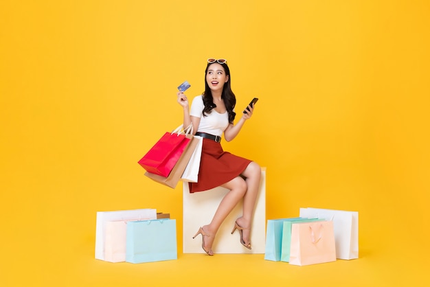 Mujer llevando bolsas de compras con tarjeta de crédito y teléfono móvil en manos