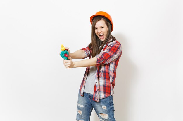 Mujer loca irritada en ropa casual y casco naranja de construcción protectora con taladro de juguete aislado sobre fondo blanco. Instrumentos, herramientas para la renovación de la habitación del apartamento. Reparar el concepto de hogar.