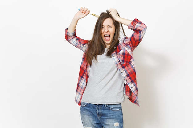 Mujer loca irritada en ropa casual pintando el cabello con pincel, aferrándose a la cabeza y gritando aislado sobre fondo blanco. Instrumentos para la renovación de la habitación del apartamento. Reparar el concepto de hogar.