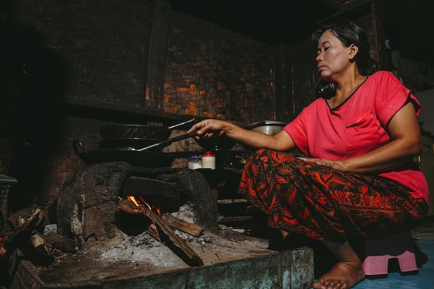 La mujer local asiática está cocinando en una estufa tradicional en la cocina del cubículo de madera