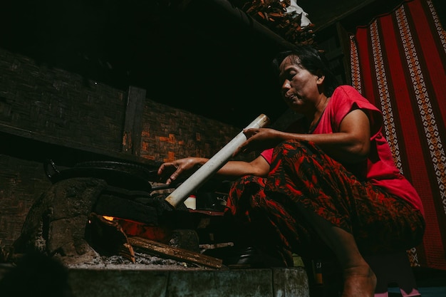 La mujer local asiática está soplando la chimenea para cocinar en su cocina tradicional