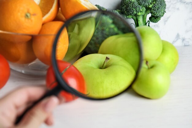 Mujer con lupa explorando verduras y frutas primer plano Detección de veneno