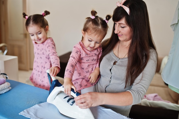 La mujer madre y sus dos hijas, niñas, ayudan a planchar en casa.