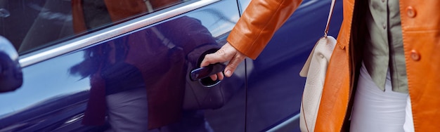 Mujer madura abre la puerta del coche púrpura de pie en las calles de la ciudad closeup