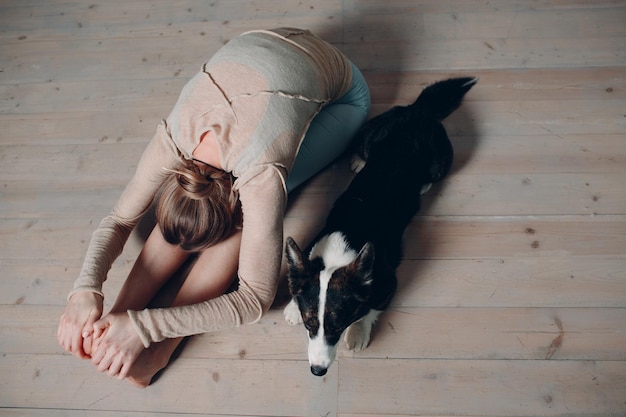 Mujer madura adulta haciendo yoga en casa en el salón con mascota perro corgi