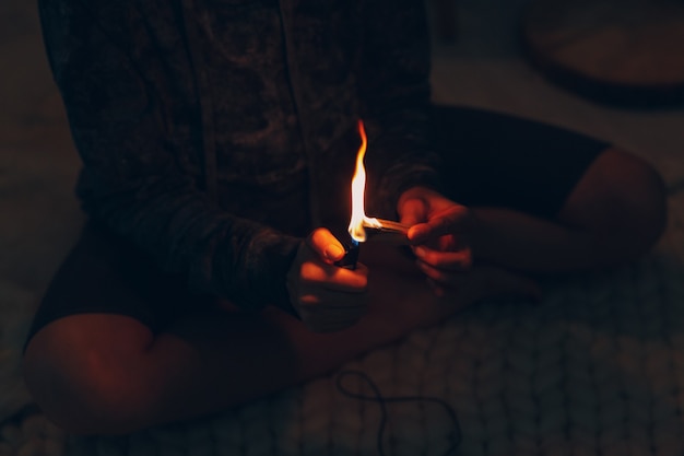 Mujer madura adulta haciendo yoga en casa salón prende fuego con incienso de palo de palo santo