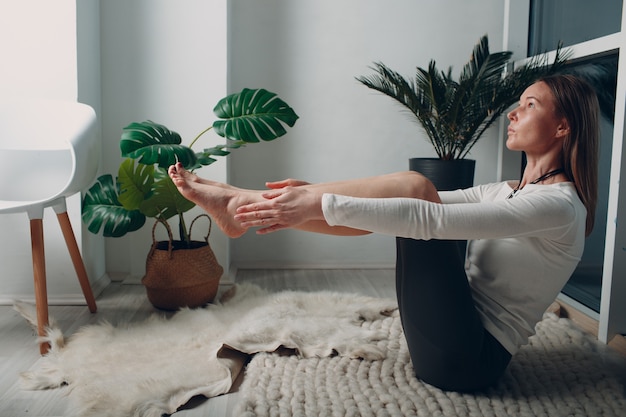 Foto mujer madura adulta haciendo yoga en la sala de estar de casa con tutoriales en línea en la computadora portátil