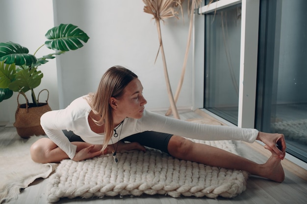 Mujer madura adulta haciendo yoga en la sala de estar de casa con tutoriales en línea en la computadora portátil