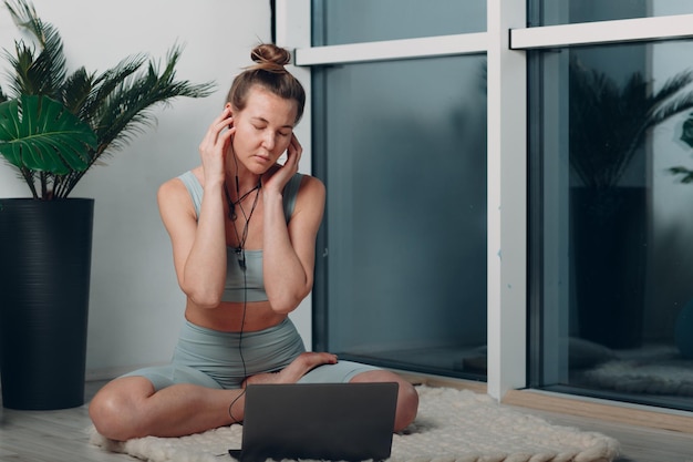 Mujer madura adulta haciendo yoga en la sala de estar de casa con tutoriales en línea en la computadora portátil