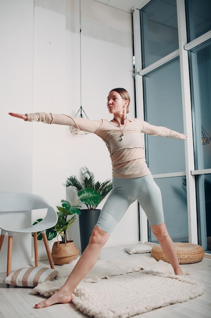 Mujer madura adulta haciendo yoga en la sala de estar de casa con tutoriales en línea en la computadora portátil