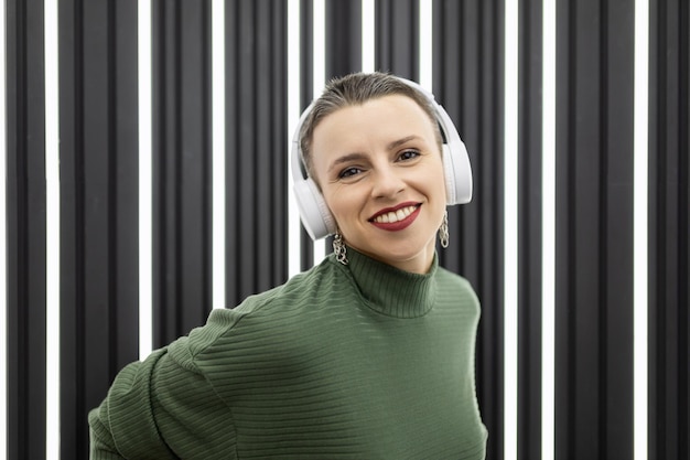 Una mujer madura alegre con un corte de pelo corto en los auriculares con una amplia sonrisa en el fondo de un