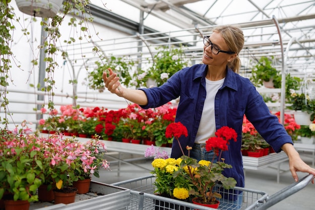 Mujer madura alegre mirando flores en el centro de jardinería