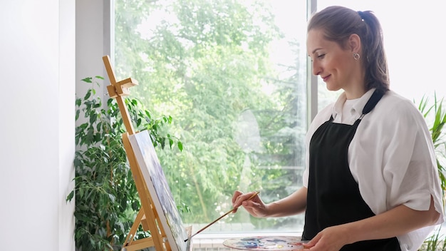 Mujer madura artista pinta cuadro sonriendo en primer plano de caballete