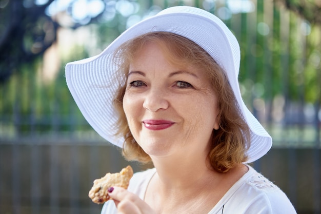 Mujer madura atractiva con sombrero está planteando al aire libre dama caucásica de mediana edad en tocado está sonriendo