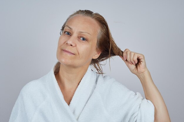 Mujer madura en bata de baño blanca con el pelo mojado después de la ducha