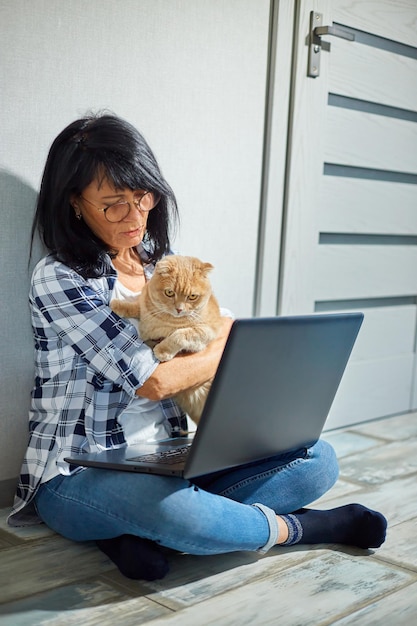 Mujer madura buscando en el sitio web veterinario en una laptop para registrar un gato para una consulta veterinaria