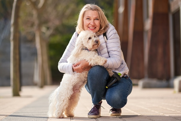 Mujer madura caminando con un perro blanco esponjoso en la ciudad de verano.