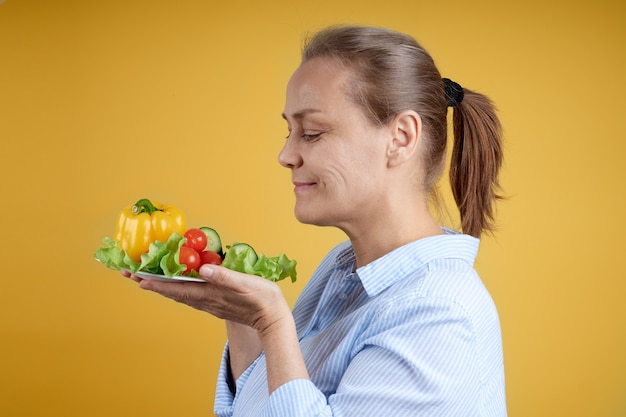 Mujer madura con una camisa blanca sostiene un plato de verduras