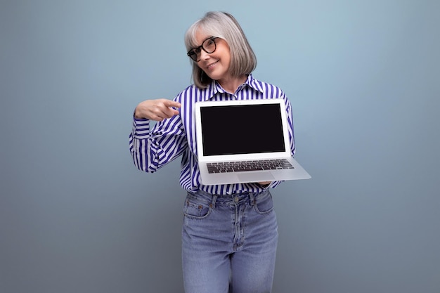 Mujer madura con canas domina profesiones remotas en línea usando una computadora portátil en un estudio brillante