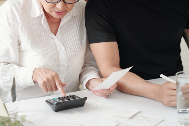 Mujer madura comprobando facturas y recibos y calculando gastos cuando se sienta junto al hijo adulto