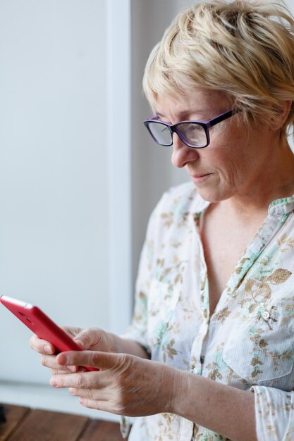 Mujer madura confiada en gafas mirando la pantalla del teléfono inteligente