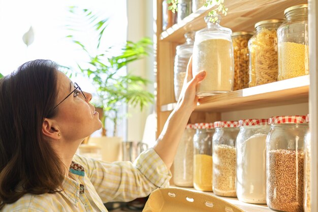 Mujer madura en la despensa de la cocina con productos