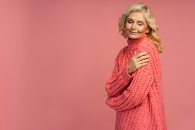 Mujer madura con elegante suéter de invierno aislado de fondo rosa. concepto de compras