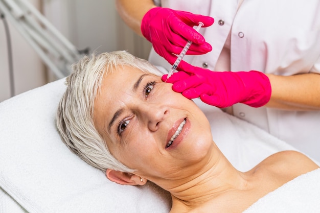 Mujer madura está recibiendo inyecciones botulínicas rejuvenecedoras faciales.