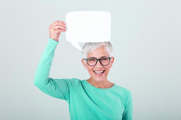 Foto mujer madura feliz con una camiseta de manga larga azul plana sosteniendo una burbuja de habla vacía aislada en el fondo mujer mostrando una pancarta de burbujas de habla de señas pareciendo feliz y señalando con el dedo