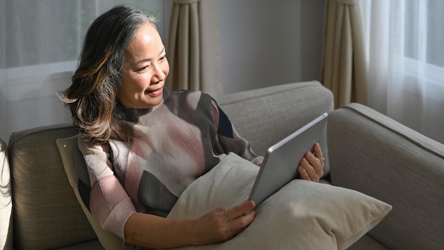 Mujer madura feliz leyendo noticias en línea revisando las redes sociales en la tableta Concepto de tecnología para ancianos