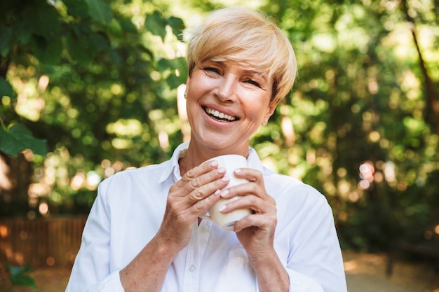 Mujer madura feliz que sostiene la taza de café