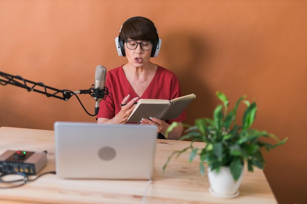 Mujer madura grabando podcasts para su programa en línea Mujer de negocios atractiva usando auriculares frente al micrófono para una persona de transmisión de radio